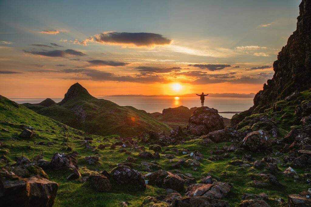 A man on a mountaintop at sunset with arms raised toward heaven